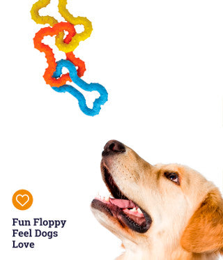 Dog looking up at a colorful bone-shaped toy with 'Fun Floppy Feel Dogs Love' text.